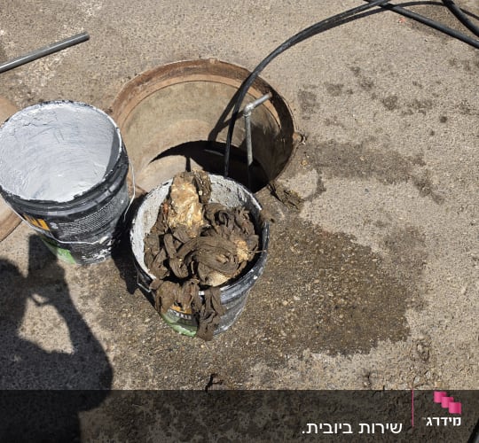 דלי עם פסולת ליד פתח ביוב וכלי עבודה